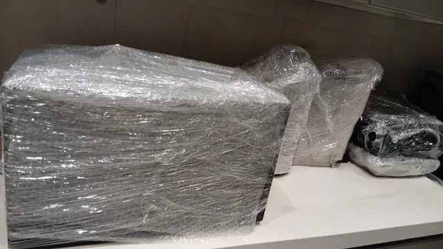 جهاز كبير قائم مغلّف بفيلم التغليف وبجانبه أغراض مغلّفة